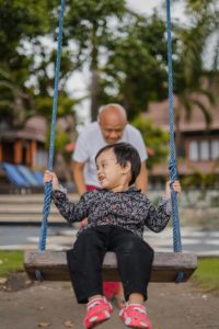 child being pushed in a swing by adult