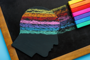 A chalkboard with a silhouette of a face. Rainbow chalk colors are coming out of the brain.