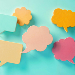 Several pastel-colored speech bubble shapes in soft yellow, pink, orange, and teal are scattered across a light turquoise background, symbolizing different voices, ways of speaking, and communication styles.